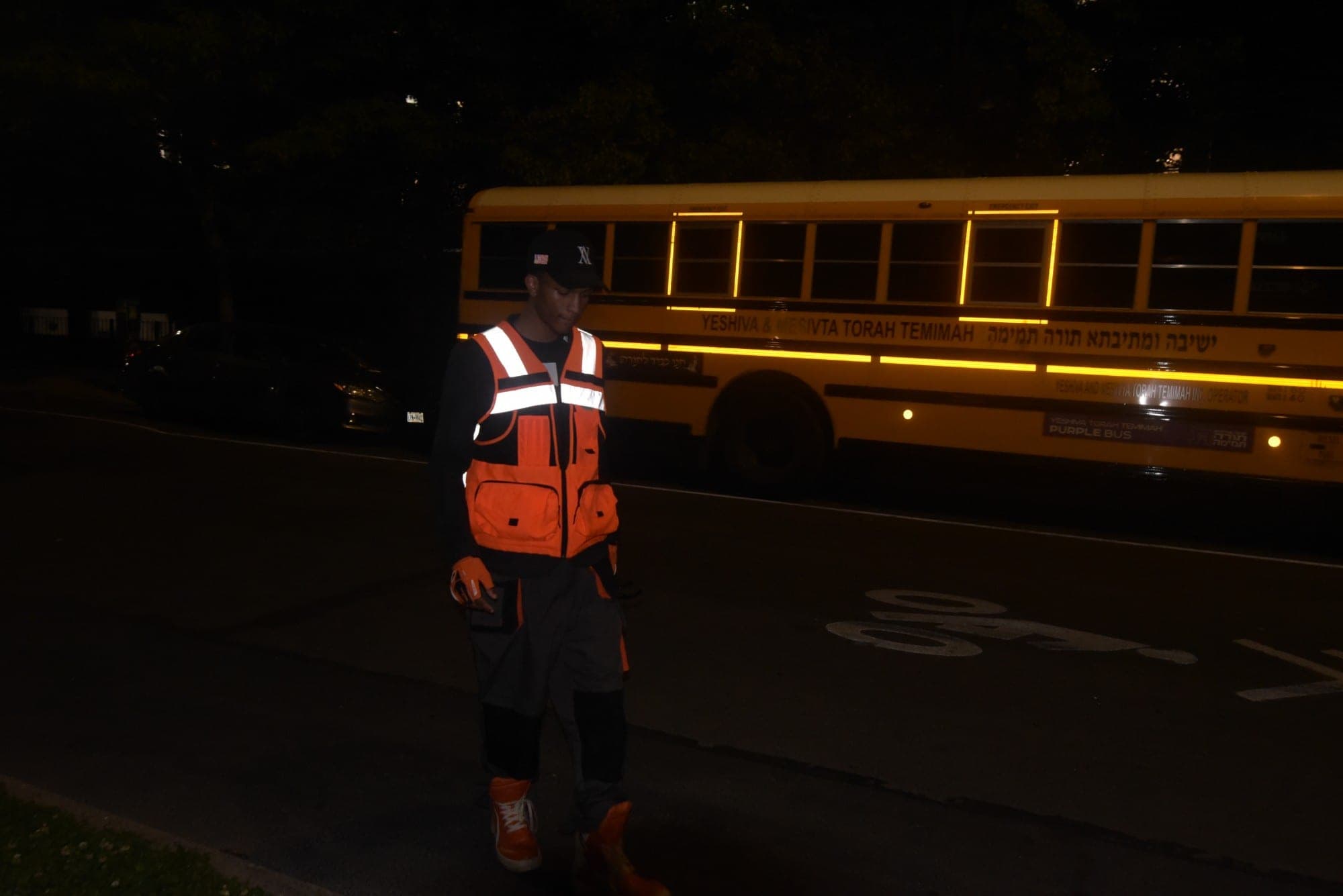 SNVRK in hi-vis workwear on a dark street in front of a school bus